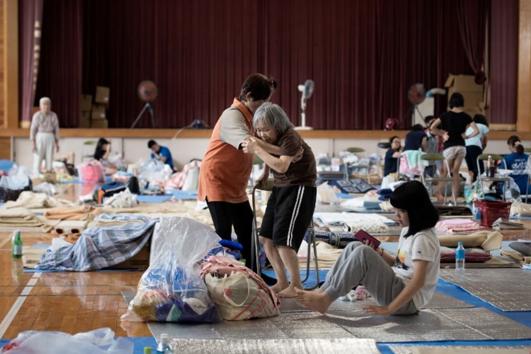 An elderly woman is given assistance as people affected by the recent flooding rest at a makeshift shelter in Mabi, Okayama prefecture on 11 July, 2018.