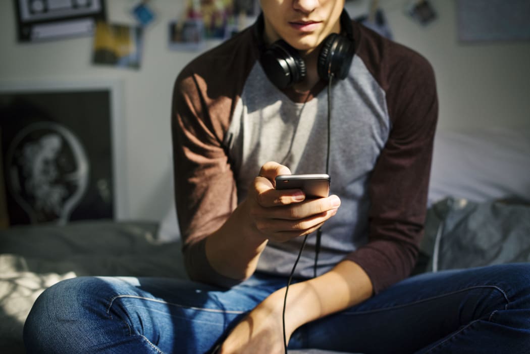Teenage boy in a bedroom listening to music through his smartphone.