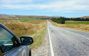 Side of car and empty road ahead with blue sky