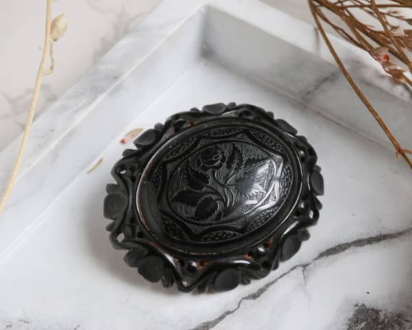 A carved black broach sits on white marble.