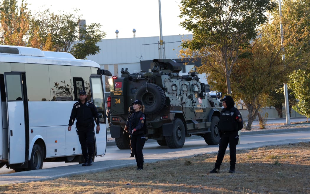 Turkish police officers gather as an armed personnel vehicle drives along a road in Kahramankazan, some 40 kilometers (25 miles) north of Ankara on October 23, 2024, near the gate of the Turkish Aerospace Industries (TAI), after a huge explosion outside the headquarters left a number of people "dead and injured", Turkey's interior minister said, describing it as a "terrorist attack". (Photo by Adem ALTAN / AFP)