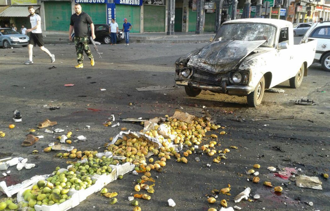 A picture released by the official Syrian Arab News Agency (SANA) shows a member of the Syrian security forces walking past a truck damaged in a suicide attack in Sweida.