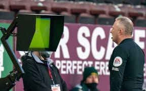 An English referee watches a VAR screen before making his ruling.
