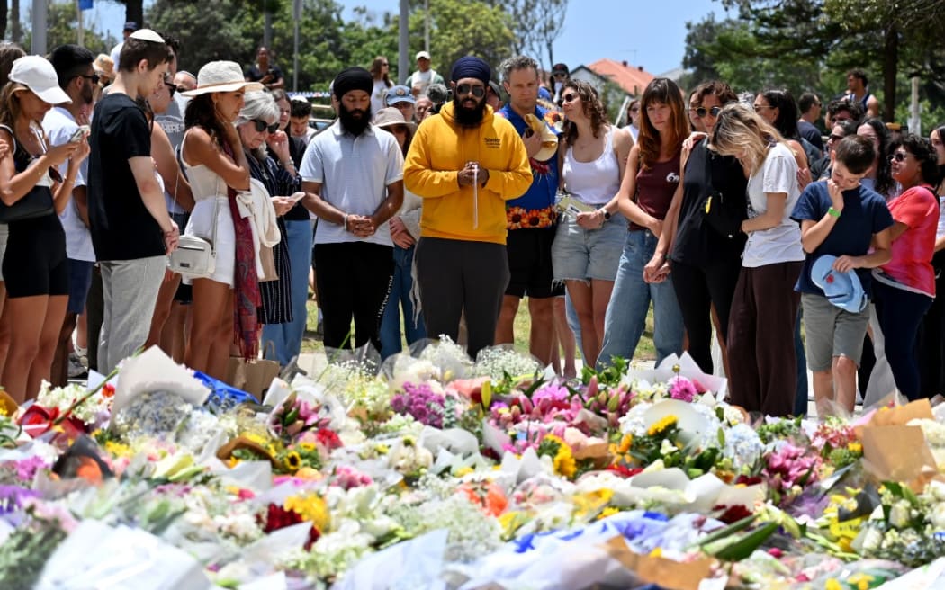 Mourners gather by floral tributes at the Bondi Pavillion in memory of the victims of a shooting at Bondi Beach, in Sydney on December 15, 2025.