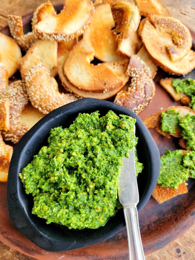 This is an image of a small bowl of bright green rocket pesto next to some toasted bagel halves.