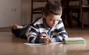 A primary school student does his homework on the floor at home.