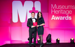 ​Simon Gould, Head of Exhibitions accepting MOTAT'S award from MC and BBC host Ella Al-Shamahi.