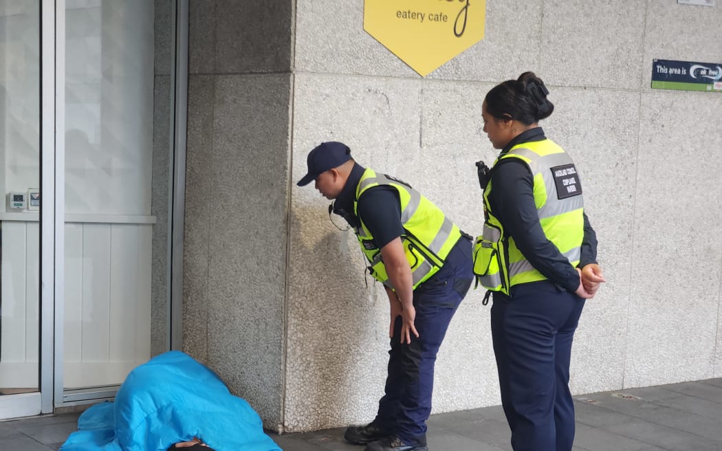 Auckland Council patrollers try to wake up a rough sleeper.