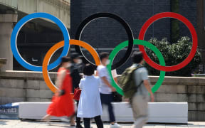 Pedestrians pass before a large monument of the Olympic rings in Tokyo
