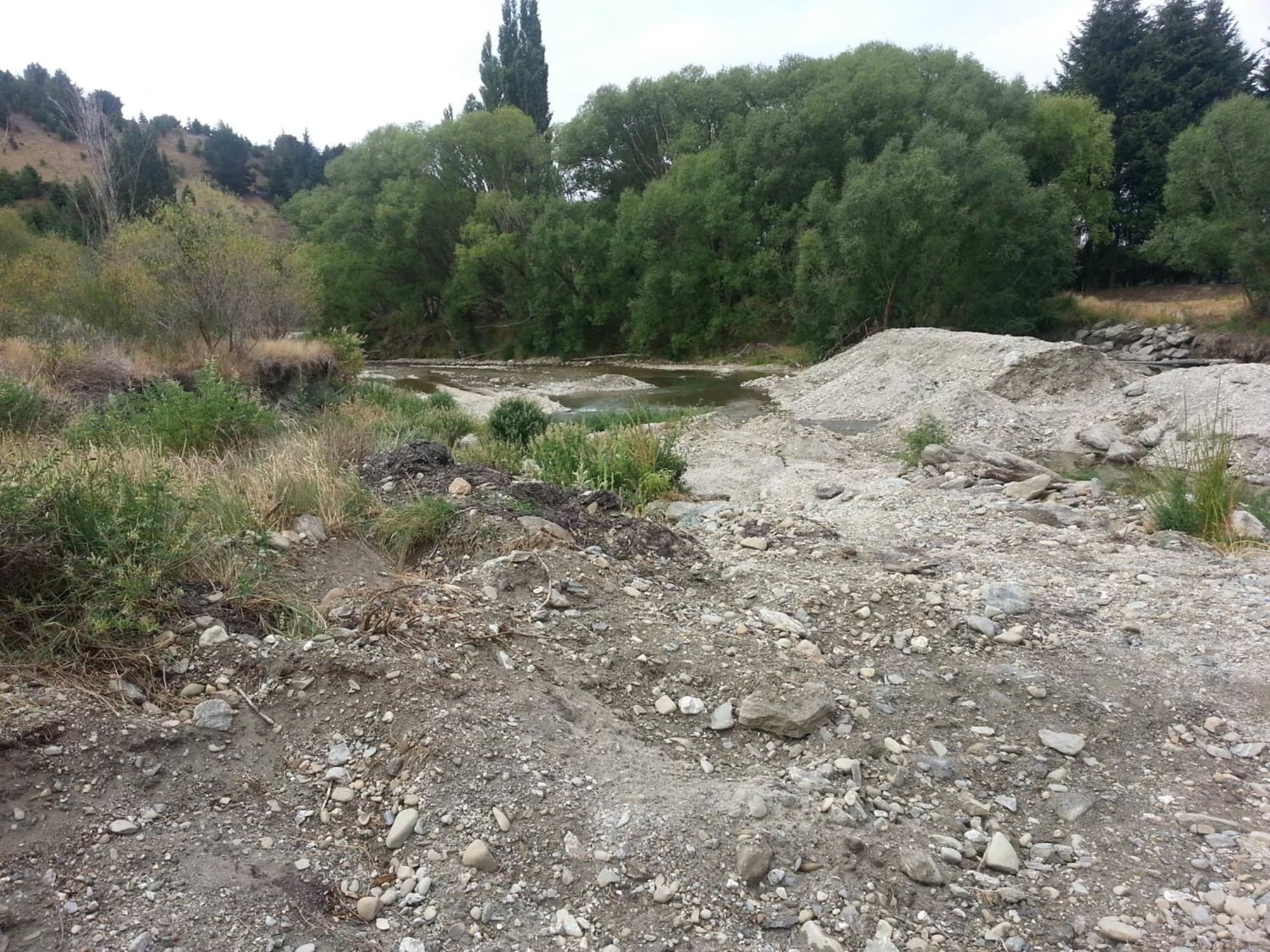 Rubble of a dry rive bed with brown water in the background