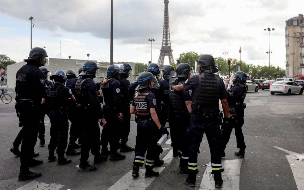 Police officers gather as clashes with crowd erupt following the PSG team bus parade, near the Champs-Elysees avenue with the Eiffel Tower in the background in Paris on June 1, 2025, a day after PSG won the 2025 UEFA Champions League final football match against Inter Milan in Munich. (Photo by Romain PERROCHEAU / AFP)