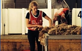 Woman with red tabbard top on sorting wool on a table in the shearing shed