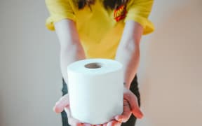 A person holds out a roll of toilet paper.
