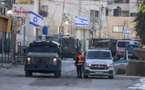 Israeli forces in armoured vehicles stop a Palestinian ambulance for a search as they block a road during a raid in Jenin in the occupied West Bank on 21 January 2025.