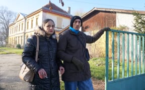 An elderly man and woman stand outside a closed down mental institution where they lived in Croatia