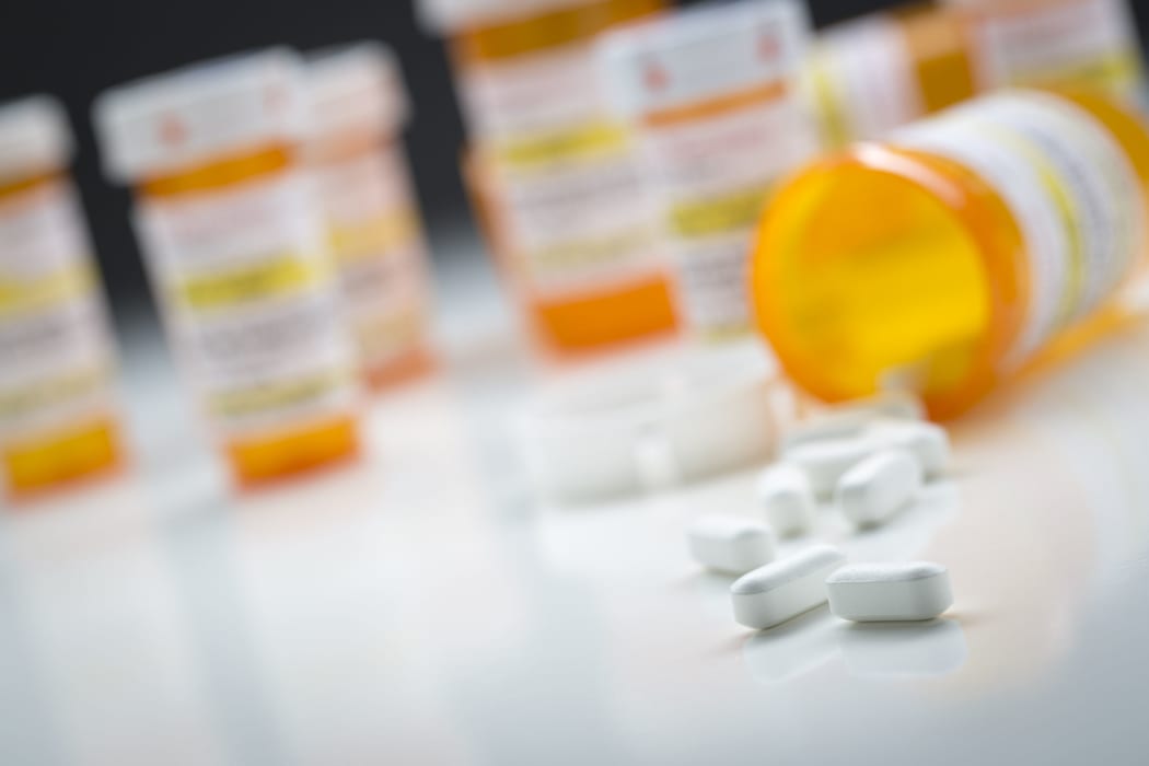 Variety of medicine bottles behind pills spilling from fallen bottle.