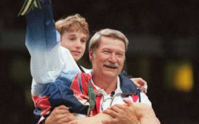 US Olympic artistic gymnastics' coach Bela Karolyi carries injured gymnast Kerri Strug onto the podium after his team won the women's gold medal 23 July at the Georgia Dome in Atlanta. The US won the event ahead of Russia and world champion Romania. (FOR EDITORIAL USE ONLY)  AFP/IOPP/Daniel GARCIA (Photo by DANIEL GARCIA / AFP)