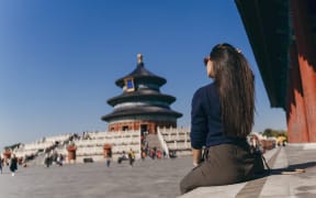brunette girl sitting on the steps by temple of heaven in China. Brunette girl enjoying chinese architecture while sitting on the steps and relaxing. Caucasian tourist taking a break from exploring Beijing China by taking some time to herself.