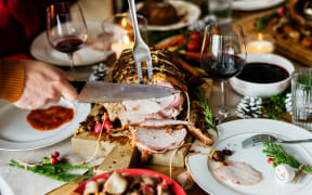 A person slicing roasted ham on a dinner table full of food plates and wine.
