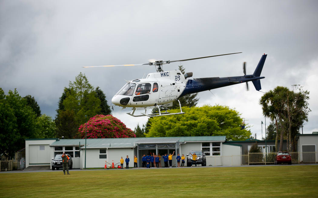 Tongariro fire - 10 November 2025. FENZ District Commander Nigel Dravitzski leaving National Park School grounds in a chopper while school children watch from outside their classroom