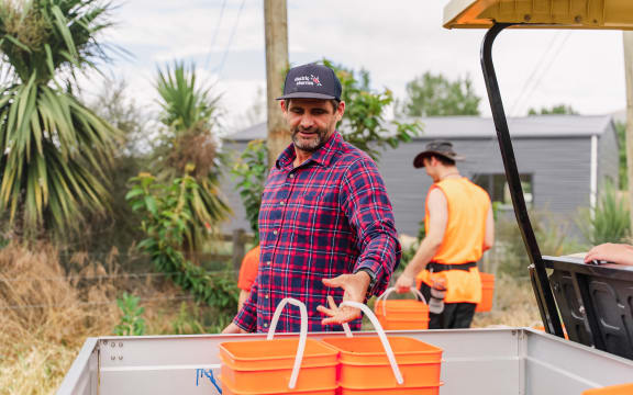 Mike Casey places two large orange buckets in the tray of a farm vehicle