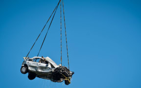 An NH90 helicopter winches the car from the Mohaka River.