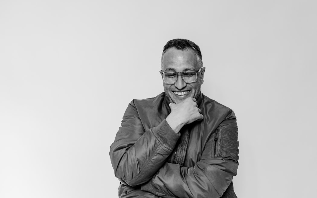 A man in a jacket smiles and rests his hand on his chin.