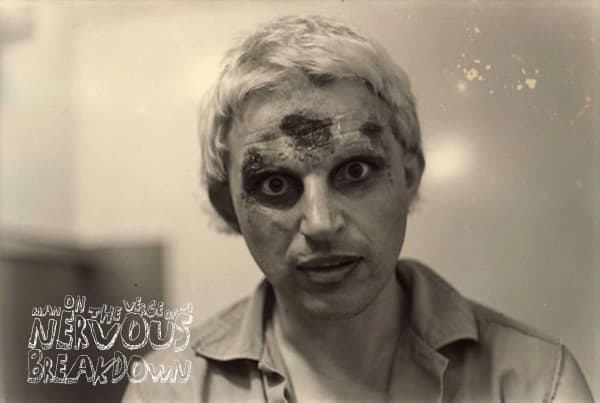 Chris Knox with white hair, ghoulish eye make-up and marks on his head that look like fake blood gives an intense look to the camera.