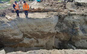 Workers in high vis clothing stand at the edge of a large hole in SH5.