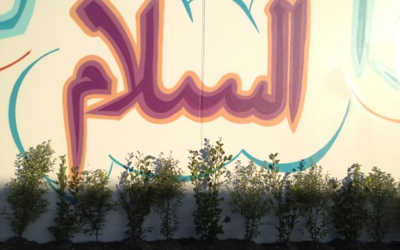 Plants in commemoration of the 51 lives lost in the Christchurch mosque shootings are put at Linwood Mosque underneath a mural of a saying from the Prophet.