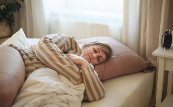 A woman lying down in bed wearing pyjamas and hugging a blanket as she falls asleep.