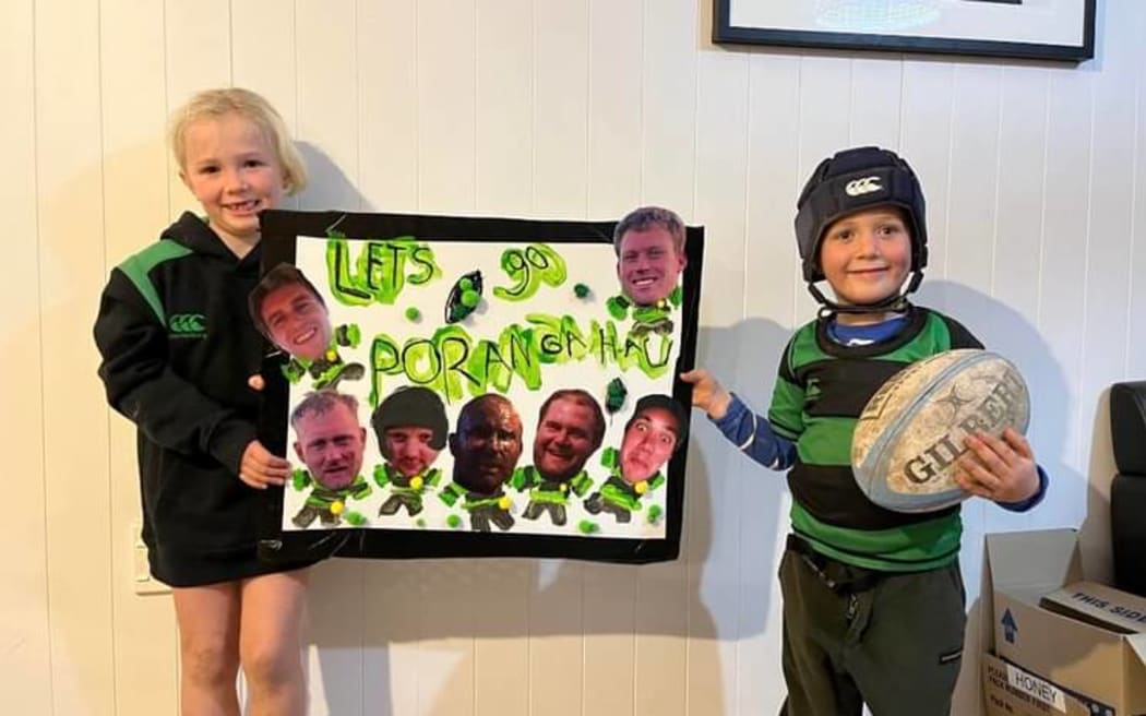 Two siblings hold up the sign lets go Porangahau!