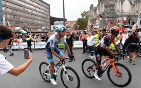 Cyclists ride back to their bus as pro-Palestinian protesters holding Palestinian and Basque flags demonstrate during the eleventh stage of the Vuelta a Espana cycling tour, on September 3, 2025.  (Photo by ANDER GILLENEA / AFP)