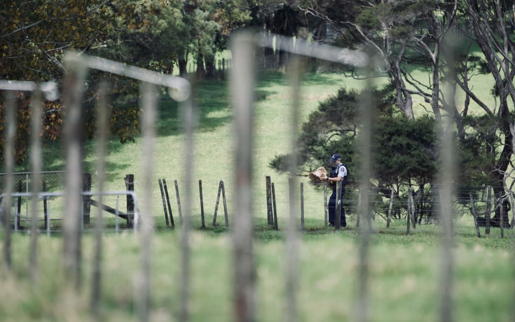 A cop walks with a bag back to a police car after two people were found dead on a rural property in West Auckland's Waitakere on 18 April 2024.