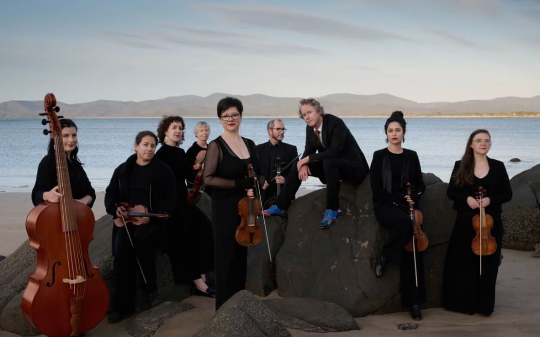 Australian early instrument ensemble Van Diemen's Band pose with instruments on a beach.