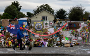 A man man walks past flowers and tributes displayed in memory of the twin mosque massacre victims along the road outside the Linwood mosque (back C) in Christchurch on March 25, 2019. The slaughter of 50 people at Friday prayers in two Christchurch mosques on March 15 shocked the normally laid-back country and prompted global horror, heightened by the gunman's cold-blooded livestreaming of the massacre. (Photo by ANTHONY WALLACE / AFP)