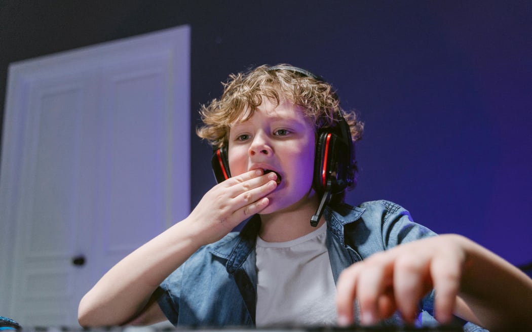 A young boy eating while gaming