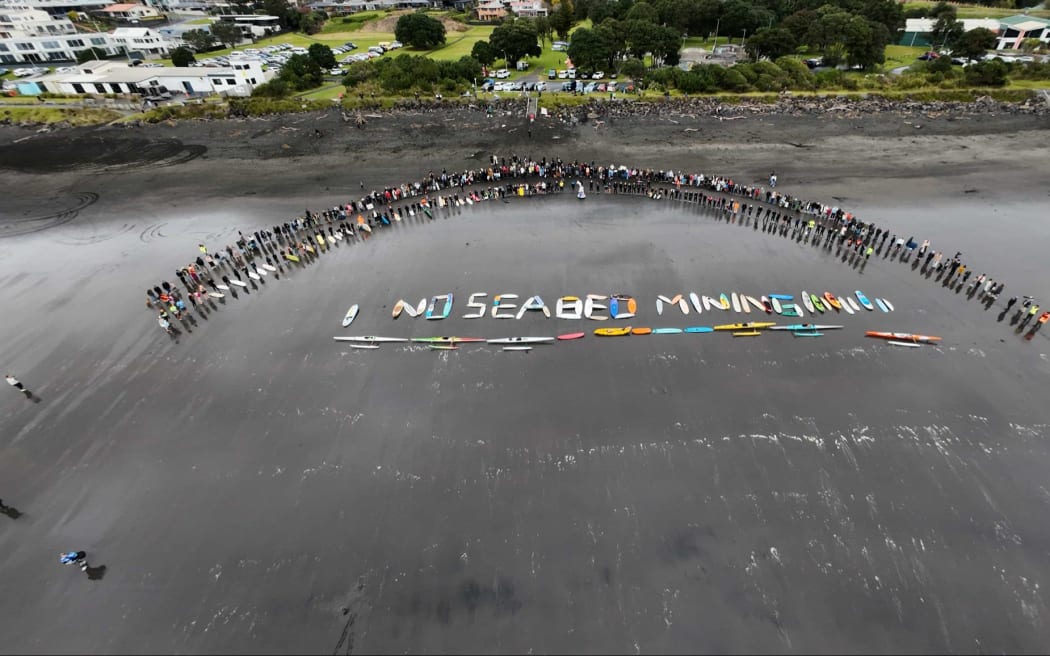 Surfboards and water craft spelled-out ‘no seabed mining’ on the black sand of Autere.