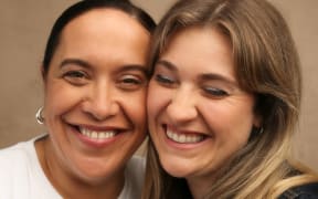 Comedians Kura Forrester and Brynley Stent laughing and smiling at the camera.