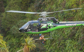 A rescuer is winched down to a hunter and his dog.