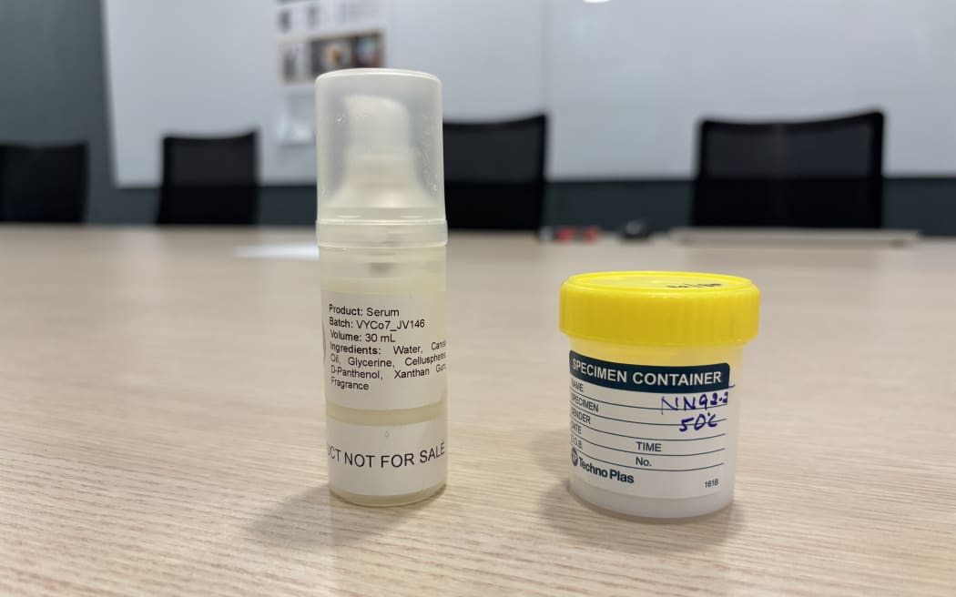 Two small plastic containers on a table. One is translucent with a white label that says serum. The other has a yellow lid, and a blue and white label that says specimen container.