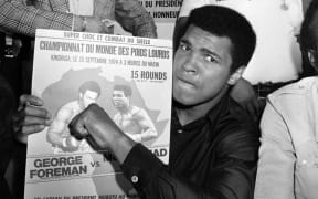 Muhammad Ali poses with a poster for his world heavyweight championship fight against titleholder US George Foreman which took place on 30 October 1974.