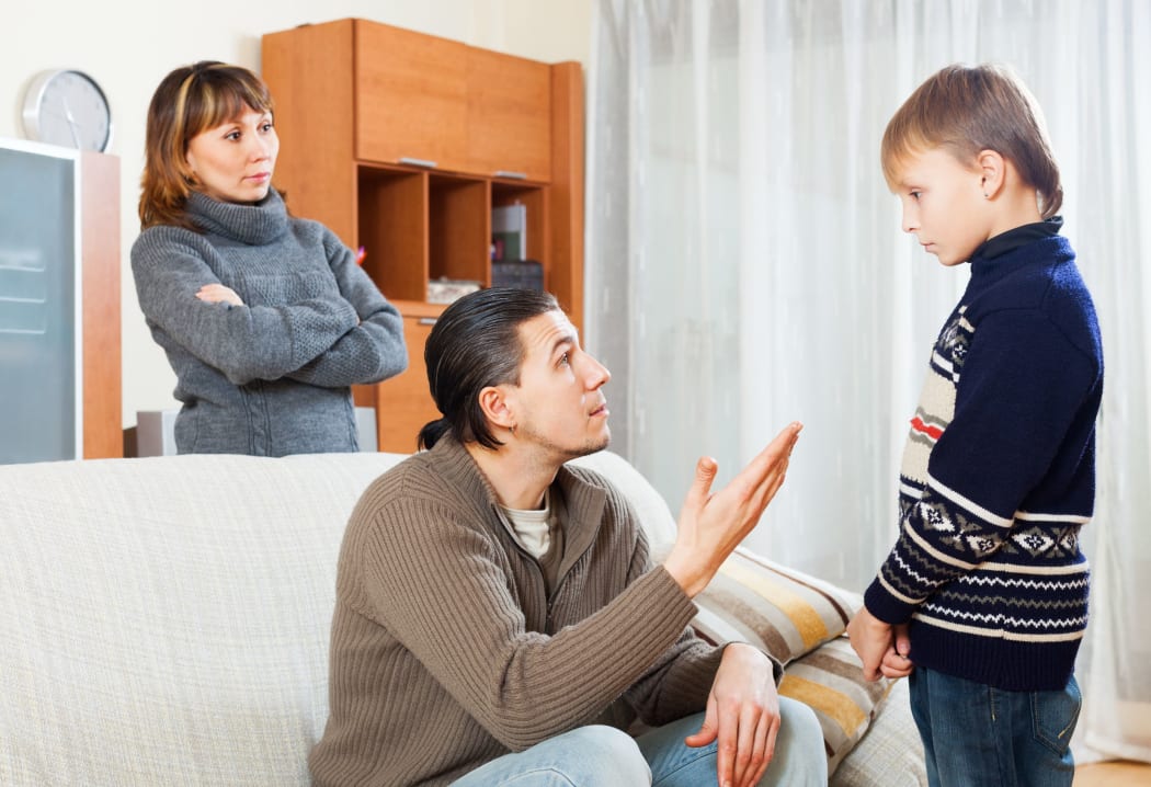A photo of serious parents berating their teenage son at home