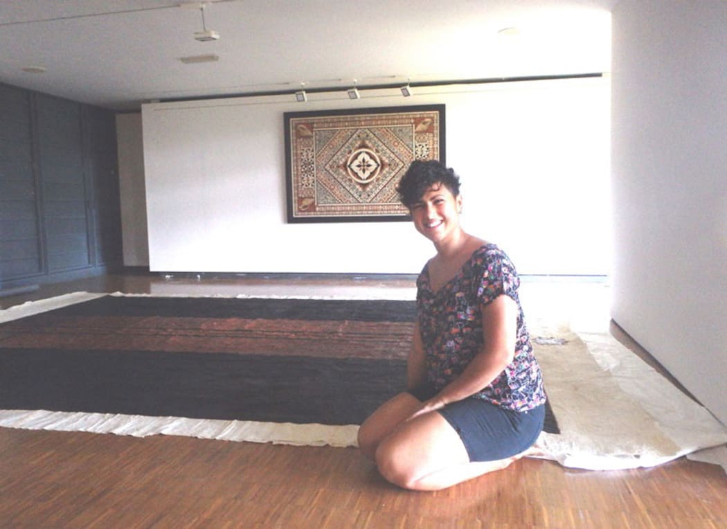 Ruha Fifita sitting in front of her enormous tapa, with another tapa by Christelle Montané on the wall.