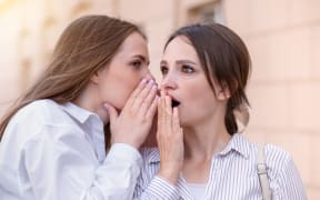 Beautiful girl says the gossip in the ear of her surprised girl