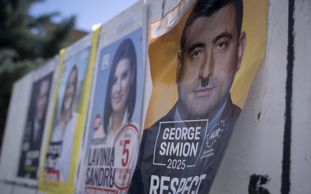 This picture shows a campaign poster of far-right front-runner George Simion (R), defaced with a graffiti depicting a toothbrush moustache, on the eve of the first round of Romania's presidential election in Giurgiu on May 3, 2025. Eleven candidates are running in Romania's presidential election first-round on May 4, a tense re-run of a vote annulled last year over claims of Russian interference. (Photo by Nikolay DOYCHINOV / AFP)