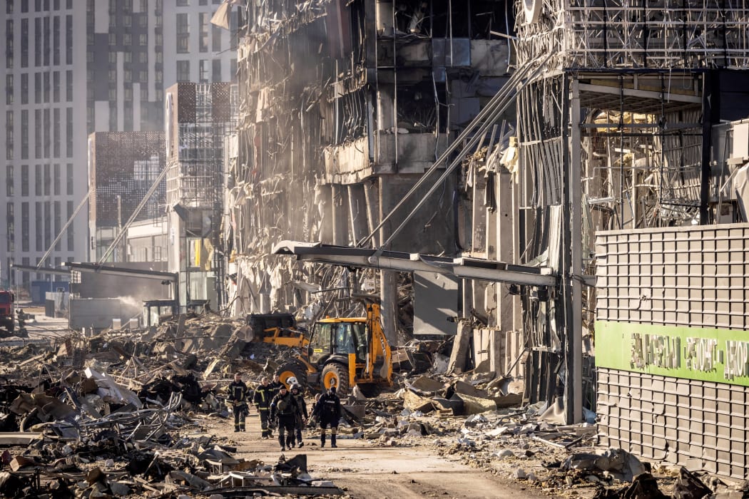 Ukrainian firefighters and servicemen work next to a digger amid the rubble of the Retroville shopping mall, a day after it was shelled by Russian forces, Kyiv, 21 March 2022.