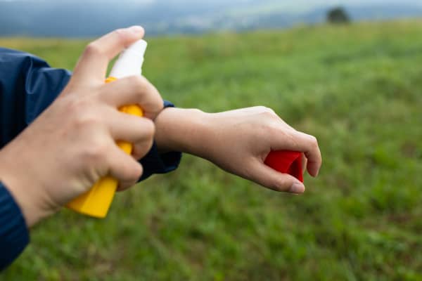 Young backpacking tourist using anti mosquito, insect repellent spray outdoors at hiking trip.