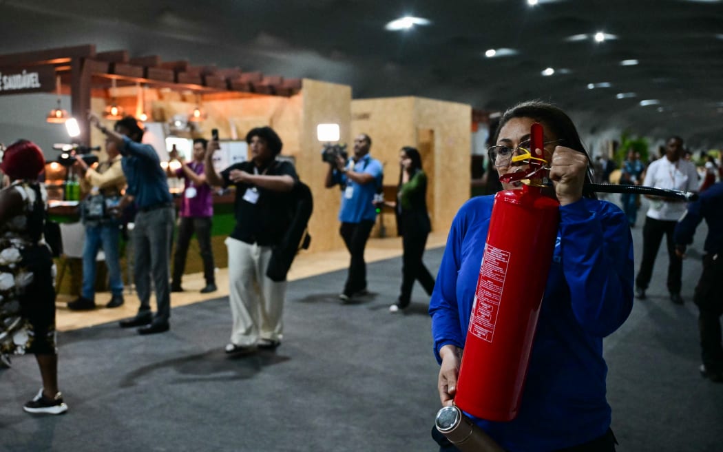 A worker runs carrying a fire extinguisher toward a pavilion after a fire broke out during the COP30 UN Climate Change Conference in Belem, Para state, Brazil on November 20, 2025. A fire erupted at a pavilion inside the venue of the UN's climate talks in Brazil on Thursday, prompting panicked delegates to run for the exits, AFP journalists said. Emergency crews rushed to try to put out the blaze as smoke engulfed the corridor. (Photo by Pablo PORCIUNCULA / AFP)