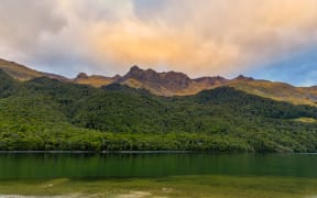 Forests and mountains surrounding North Mavora Lake at sunset on a cloudy day.